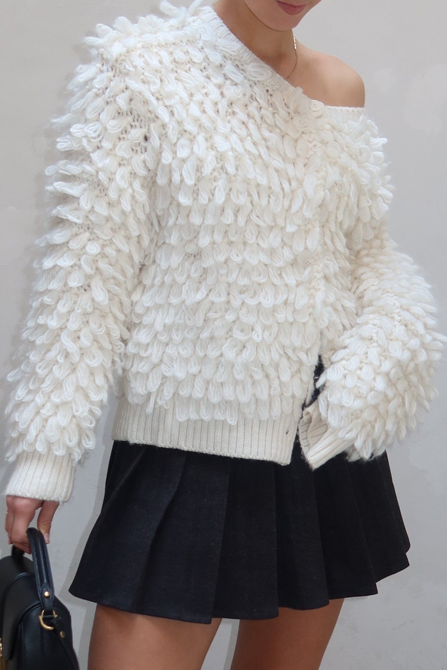 Person wearing a white textured sweater, black skirt, and black boots on a light gray floor.
