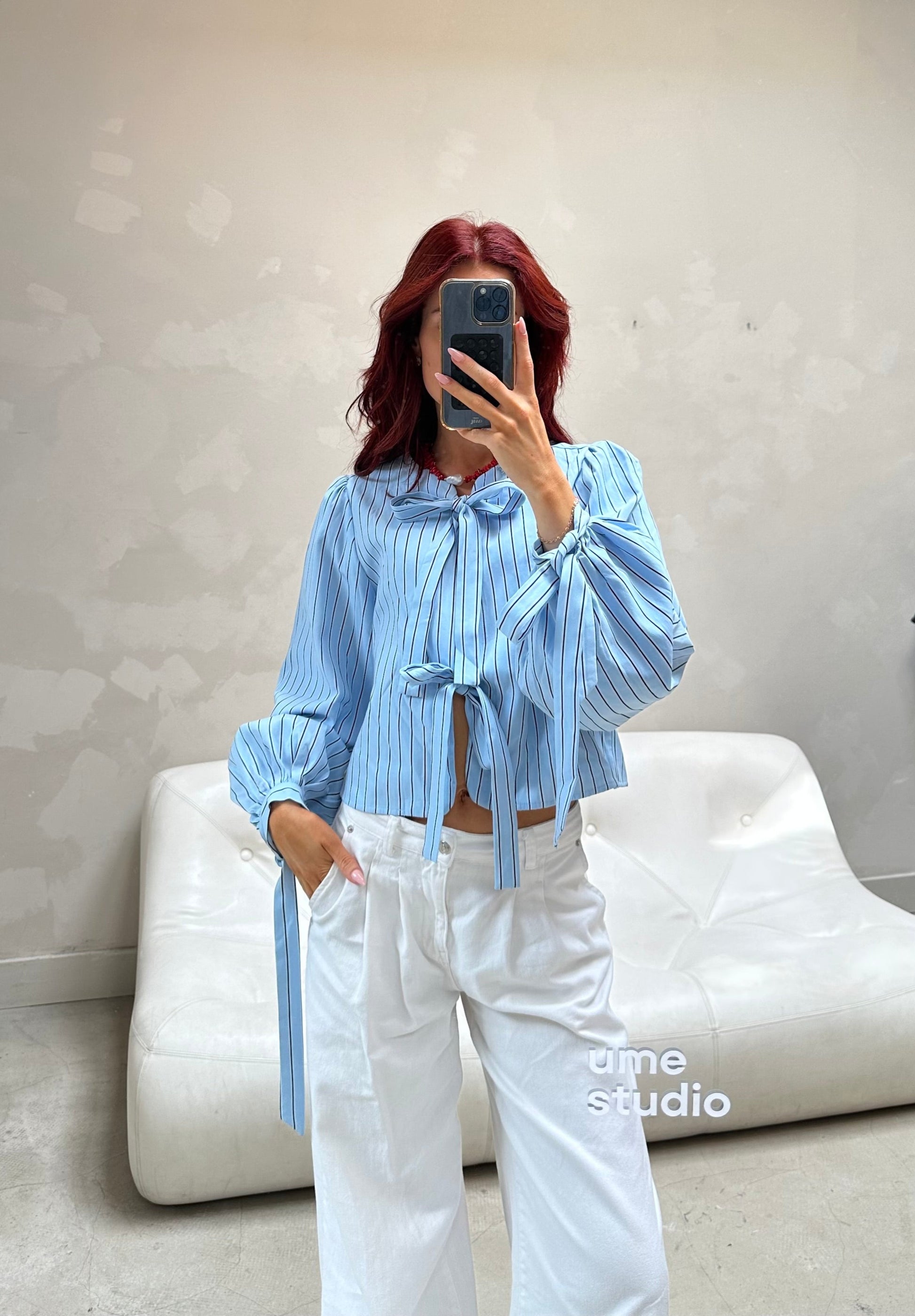 Person wearing a blue striped shirt and white pants taking a mirror selfie.