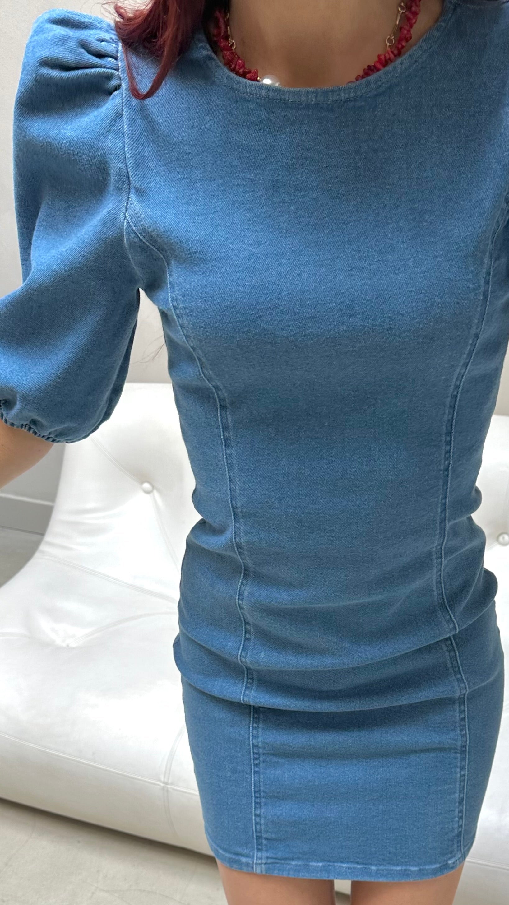 Person wearing a blue dress with puffed sleeves on a white couch.