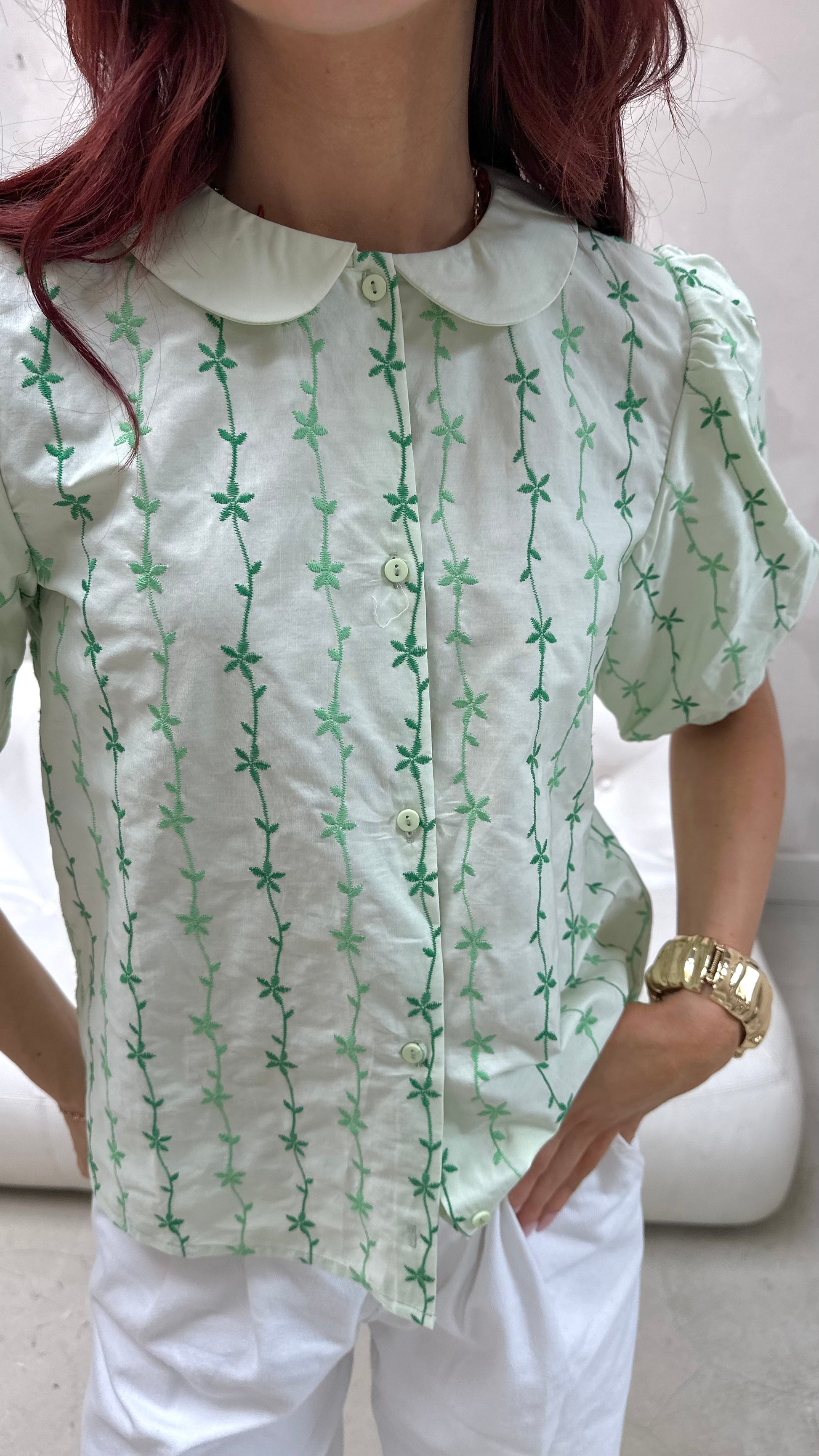 Person wearing a light green blouse with a subtle pattern, paired with white pants.