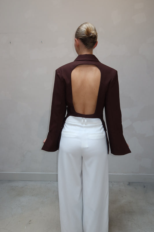 Person wearing a brown open-back top and white pants on a plain background