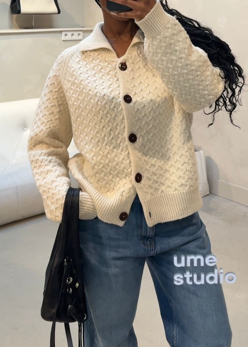 Person wearing a cream cardigan and blue jeans taking a mirror selfie in a store.