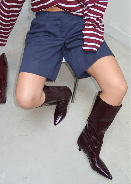 Person wearing striped pants and a skirt with brown boots on a gray floor.