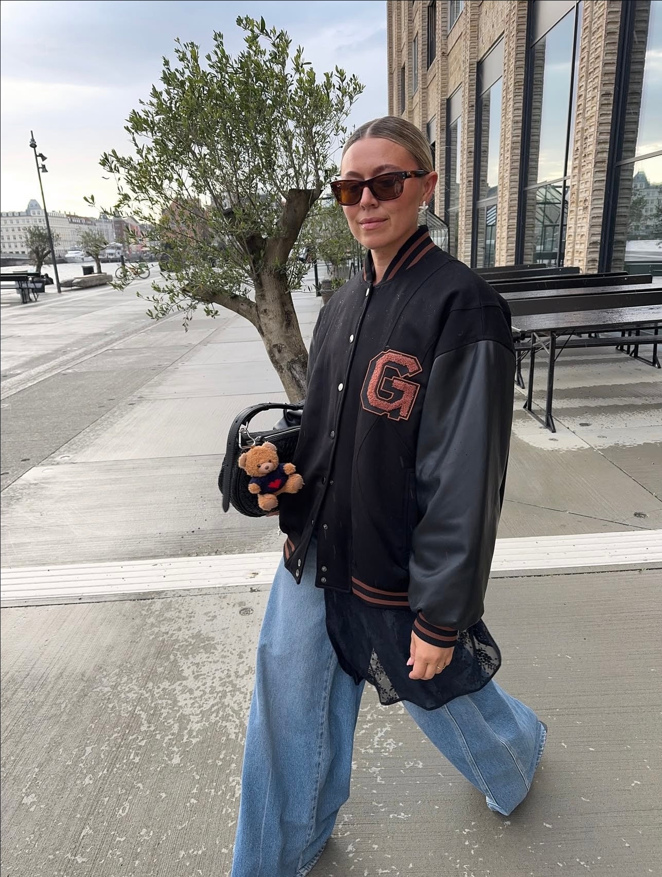 Person wearing a black varsity jacket with a red letter 'G' on a sidewalk.